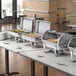 A Choice Deluxe roll top chafer on a buffet table with food.
