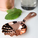 A Barfly copper julep strainer with a scalloped edge over a glass of mint leaves.