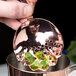 A person using a Barfly copper scalloped julep strainer to strain mint leaves into a copper cup.