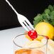 A Barfly stainless steel bar spoon with a fork end resting on a cherry in a glass of liquid.