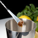 A metal cup with a Barfly stainless steel Japanese style bar spoon in it with a brown substance.