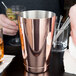 A person using a Barfly copper-plated cocktail shaker tin to make a drink.
