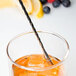 A Barfly stainless steel double end stirrer in a glass of whiskey with a straw and berries.