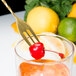 A Barfly gold plated bar spoon with fork end stirring a cocktail with a cherry and a lemon slice.