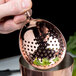A person using a Barfly copper julep strainer over a cup.