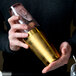 A person using a gold-plated Barfly cocktail shaker tin.