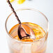 A copper Barfly classic bar spoon in a glass of liquid.