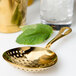 A Barfly gold-plated julep strainer over a glass of lemonade with mint leaves.