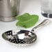 A silver Barfly stainless steel julep strainer over a glass of mint leaves.