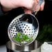 A person using a Barfly stainless steel Julep strainer to pour a drink.