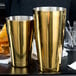 Two gold-plated Boston cocktail shakers on a table.
