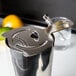 A stainless steel Barfly Hawthorne strainer on a counter with a lemon and lime.