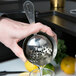 A person using a Barfly stainless steel scalloped Julep strainer to pour a drink.