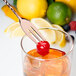 A Barfly copper plated bar spoon with a fork end stirring a glass of lemonade with a cherry on top.
