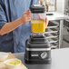 A person using a KitchenAid matte black and silver blender to make a yellow smoothie.