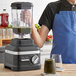 A person in a blue apron using a KitchenAid Matte Black blender to make a green smoothie.