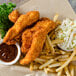 A plate of fried chicken strips and fries with coleslaw and sauce.