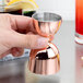 A person using a Barfly copper bell jigger to pour a shot.