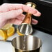 A person using a gold Barfly Japanese style jigger to pour liquid into a cup.