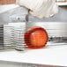 A gloved hand uses a Vollrath Tomato Pro slicer to cut a tomato on a counter.