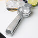 A Barfly cast aluminum citrus squeezer next to a glass of ice and fruit with a lime on the counter.