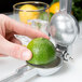 A person using a Barfly cast aluminum citrus squeezer to juice a lime into a glass of ice.