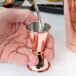 A person using a Barfly copper Japanese style jigger to pour liquid into a cup.