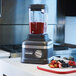 A KitchenAid commercial blender with berries and a fruit on a cutting board.