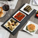 A rectangular black slate tray with plates of food and wine on a table.