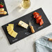 A rectangular black slate tray displaying cheddar cheese, blue cheese, and chorizo, with a cheese knife and handwritten labels.