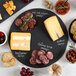 A round black slate tray displaying assorted cheeses and sausages.
