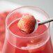 A stainless steel straw/stirrer with a strawberry on it in a glass of liquid.