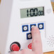 A finger pressing a button on a white digital kitchen timer.