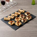 A rectangular black slate tray with pastries and soapstone chalk on it.