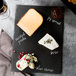 A rectangular black slate tray with cheese, wine, and crackers on it.