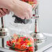 A hand using a Choice Double Canister Cereal Dispenser to pour gummy bears into a plastic bag.