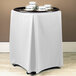 A white table with a Snap Drape Wyndham white tray stand cover on it.