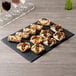 A black slate rectangular tray with pastries and wine glasses.