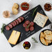A rectangular black slate tray with a variety of food including meats, cheese, olives, and nuts.