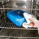 A hand using a white towel to place a lid on a blue roasting pan in an oven.