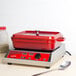 A red enamel coated cast aluminum roasting pan with a lid on a counter.
