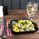 A GET black enamel coated cast aluminum mini square grill pan with food on a table.
