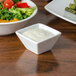 A bowl of salad next to a square white sauce cup.