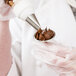 A person using an Ateco stainless steel flower nail to pipe chocolate frosting.