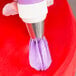 A person using an Ateco 888 swirl top piping tip with purple icing to decorate a cupcake.