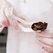A gloved hand using an Ateco white plastic flower lifter to add chocolate frosting to a spoon.