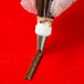 A hand using an Ateco Lily-of-the-Valley piping tip to pipe brown icing onto a chocolate stick.