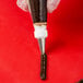 A white plastic Ateco leaf piping tip in a pastry bag with frosting on a red surface.