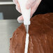A person using an Ateco leaf piping tip in a white pastry bag to frost a chocolate cake.