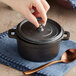 A person's hand pressing a lid onto a Valor mini cast iron pot.
